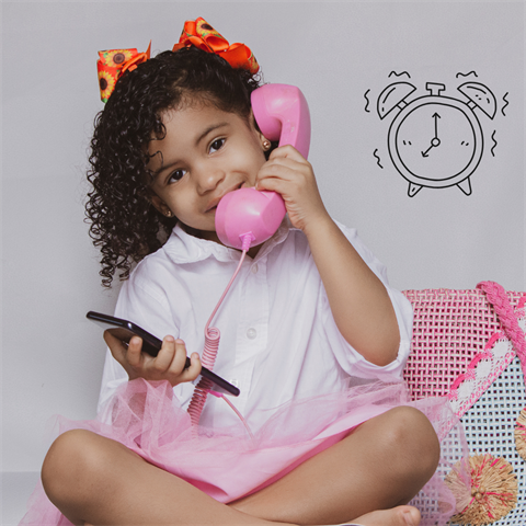 A child aged about 6 in pink listens on a pink old fashioned telephone