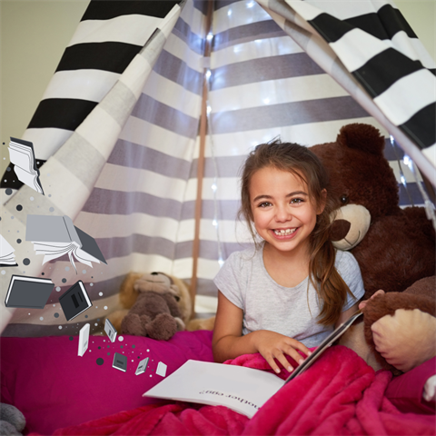 A child aged about 9 sits in an indoor tent reading a book with stuffed animals