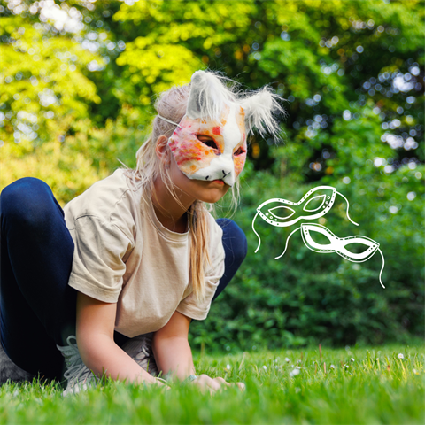 A child wearing a cat mask crouches on grass